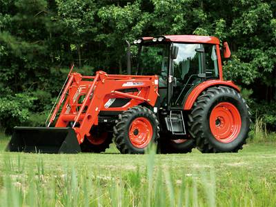 An orange and black KIOTI® PX Series tractor sitting on the grass in front of trees.